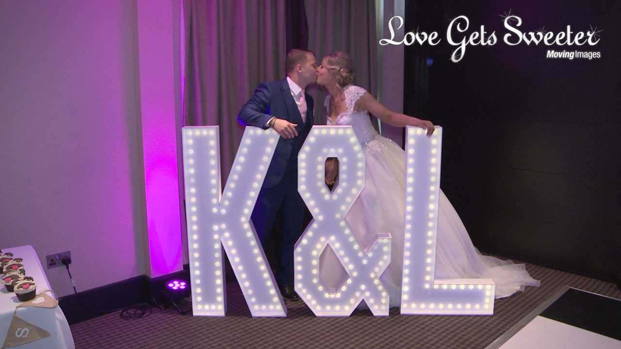 A video still of the bride and groom having a kiss whilst posing with their light up letters at their wedding in Leeds at Oulton Hall