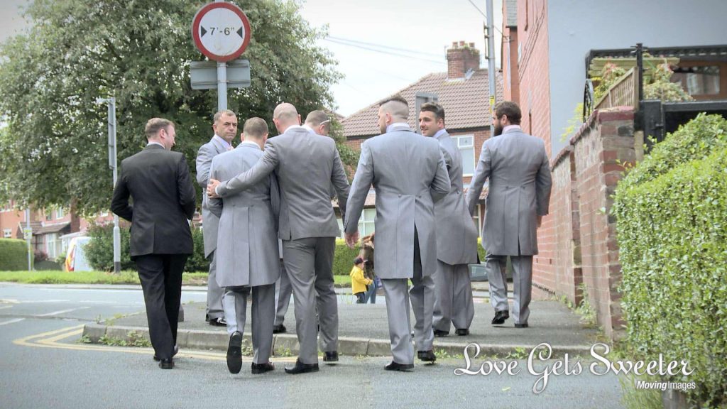 The groom and groomsmen walk down the road from his home in Middleton to the local pub before the wedding. One of them puts his arm round the groom in a supportive way