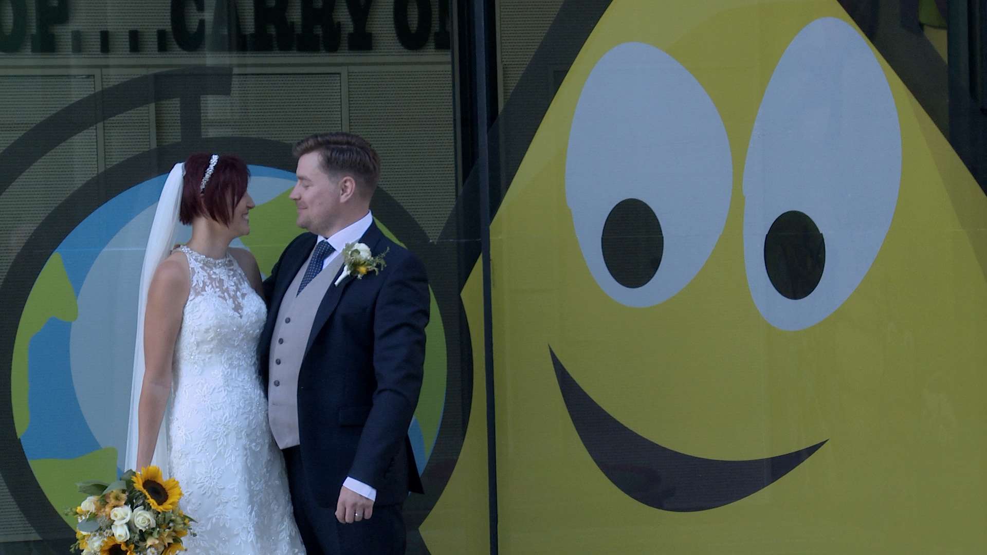 Bride and Groom standing in front of the CBeebies window in Salford Media City posing for a fun wedding photograph