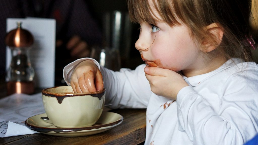 a little girl attempts to catch hot chocolate dripping down her chin as she enjoys a hot drink after a long cold walk in the lake district