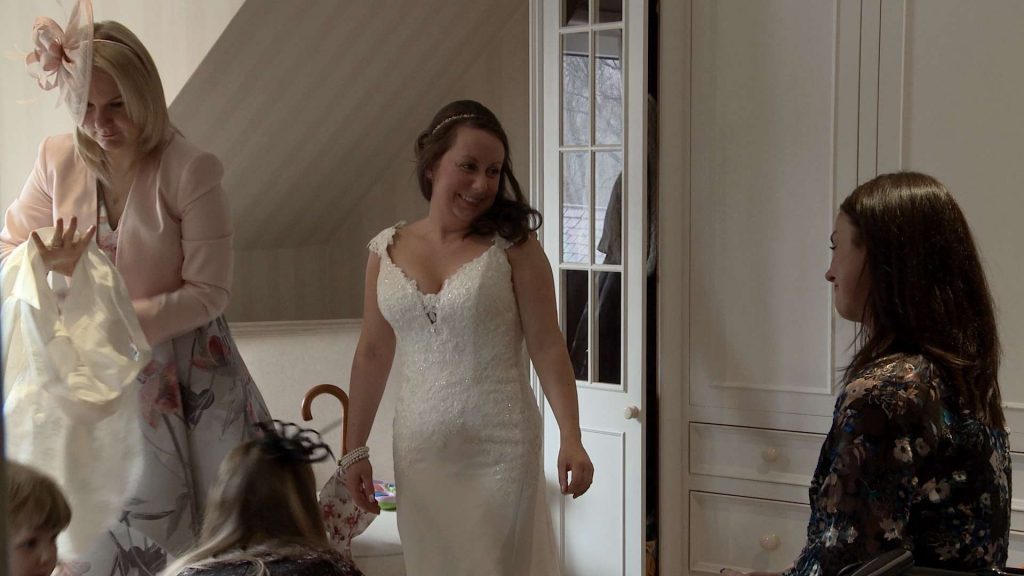 A bride shyly smiles at her best friend as she stands in her wedding dress waiting to leave for the ceremony. it looks like they're fighting back the happy tears