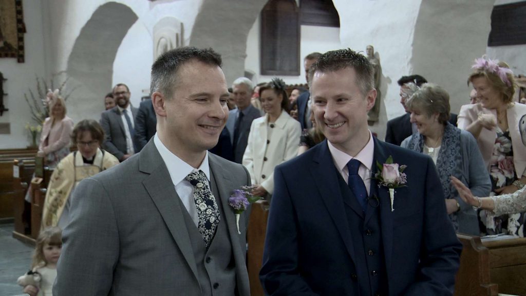 a groom and best man share a laugh standing at the front of St Oswalds church waiting for the bride to arrive