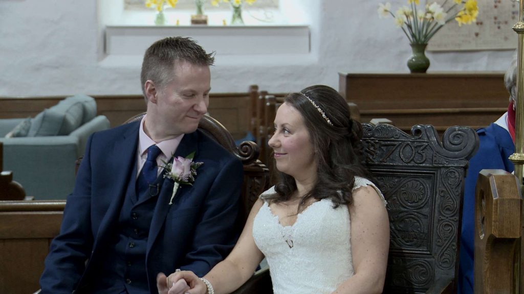 the bride and groom look at each other with a smile as they sit during their wedding ceremony in the lake district