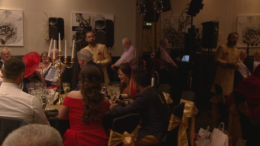 a still from the wedding video of a groom making his wedding speech to the top table at his bold hotel wedding