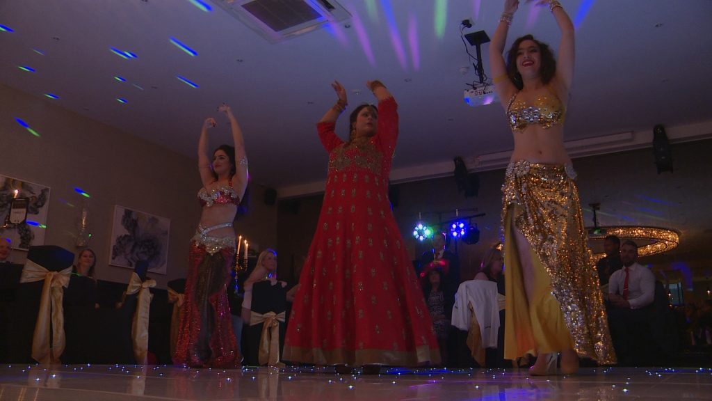 a bride in a traditional red bangladeshi wedding saree dances inbetween 2 belly dancer friends to entertain their wedding guests at the bold hotel