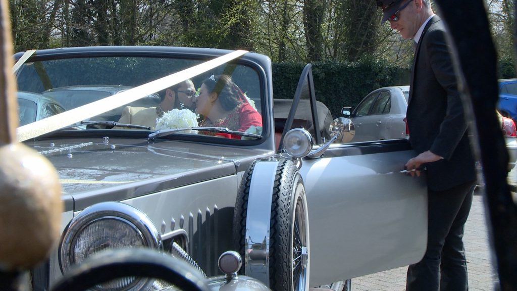 the wedding videographer captures the bride and groom having a quick kiss in their wedding car before enjoying a photo shoot in the botanic gardens in southport