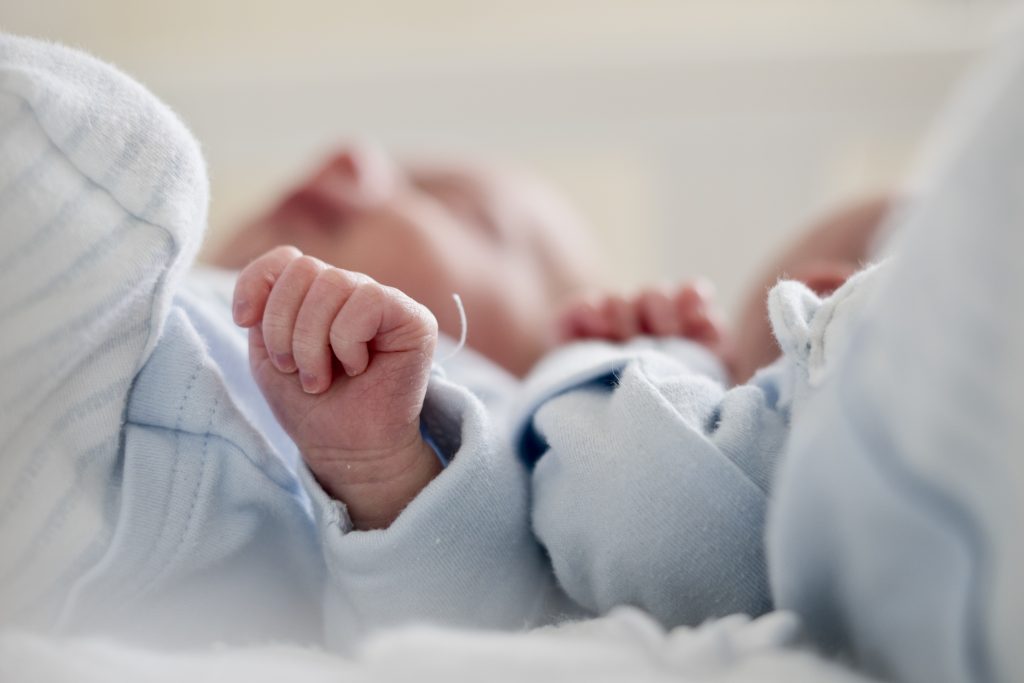 two newborn twin boys lay in their cot and the family photographer has focused on their tiny little hands