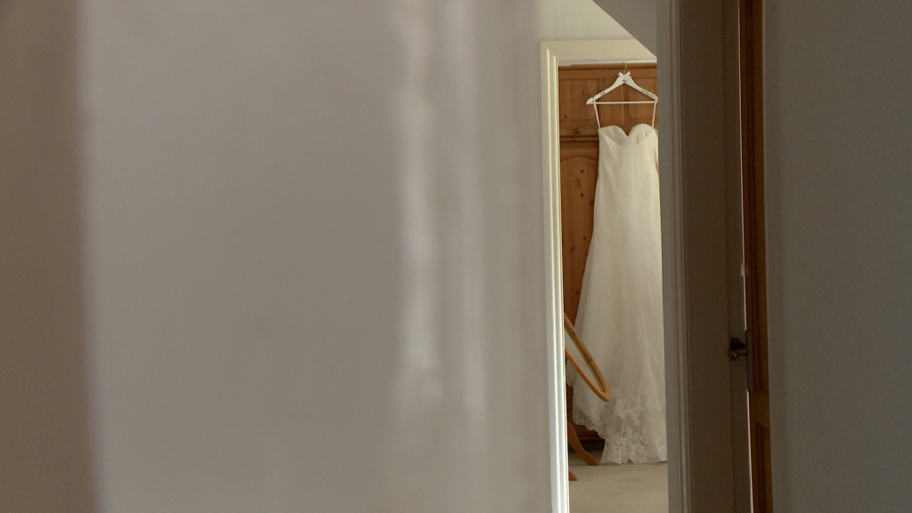 a wedding video still of a brides lace wedding dress hanging on a wardrobe in a far room like a sneak peek in her family home in Holmeswood Lancashire