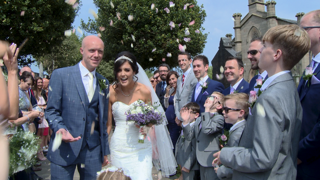 the bride laughs and ducks down as guests shower them in natural flower confetti from Dollz confetti outside St John's church in burscough