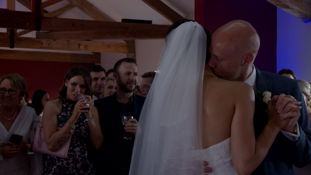 the groom gives his bride a kiss on the neck during a romantic first dance to ed sheeran at the blue mallard in lancashire for their wedding video by love gets sweeter