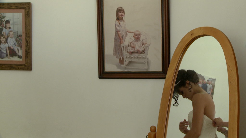 A video still from the wedding video. in the mirror you can see the bride getting in to her wedding dress and on the wall are some old vintage photographs of her as a young girl in her parents home in lancashire