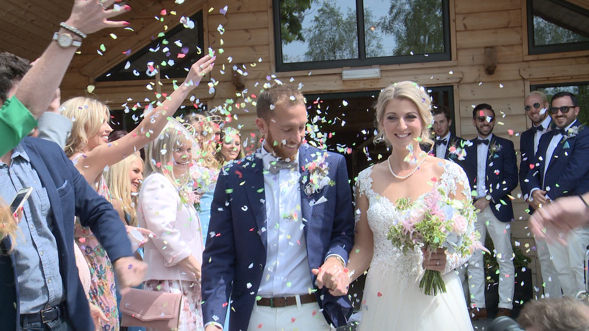 the bride and groom are showered in bright coloured natural confetti outside Styal Lodge in Cheshire for their wedding video and photos