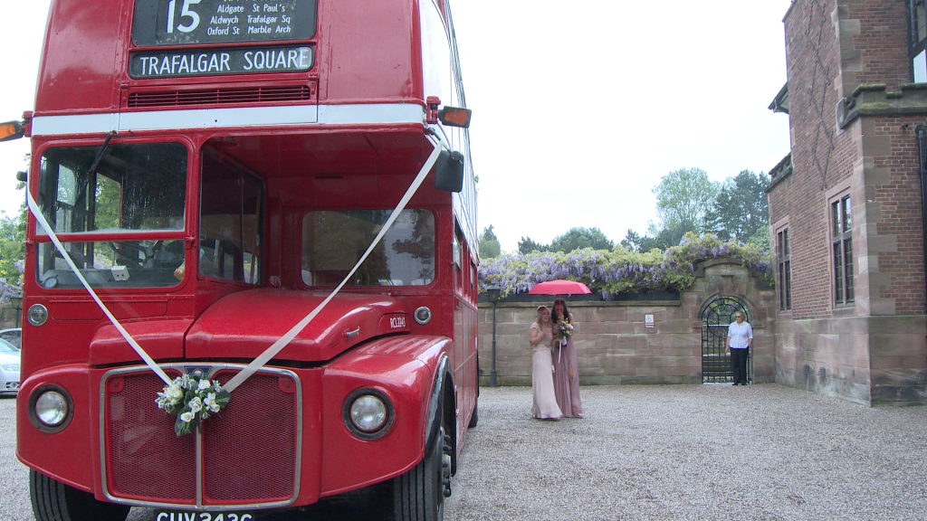 two bridesmaids hide under a red umbrella as they try to walk from the vintage london bus to the front door at Inglewood manor
