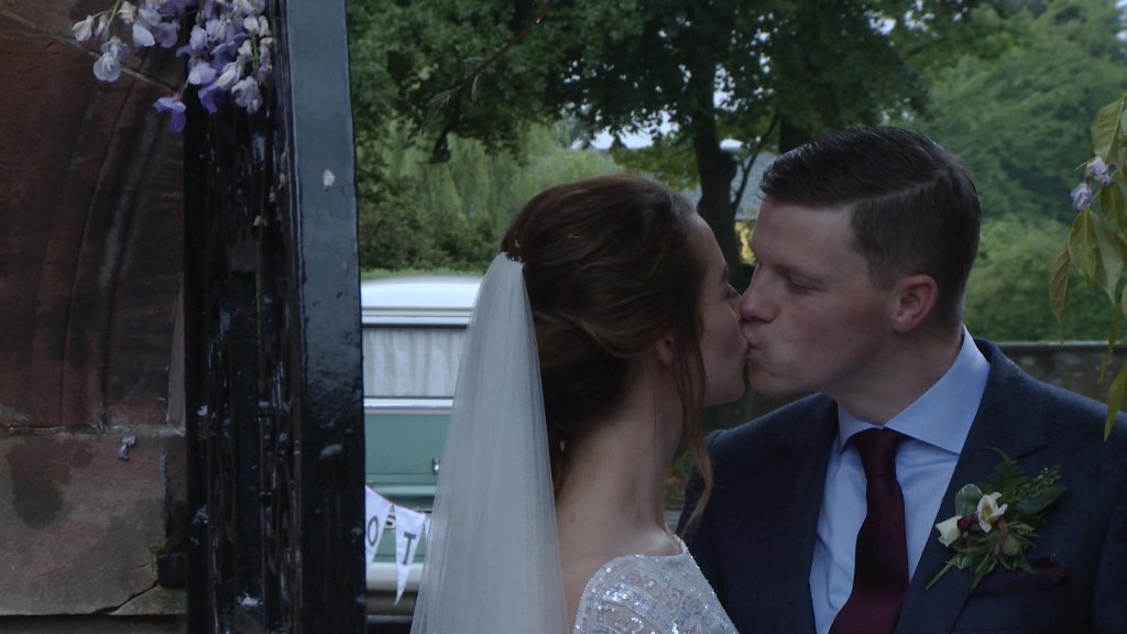 a bride and groom kiss under an archway for the photo and video at their wedding at Inglewood manor in Cheshire