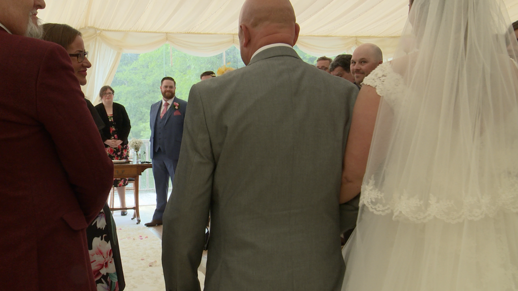 dad walks his daughter down the white carpet aisle at the lakeside marquee in thornton manor as the groom gets his first look on the wedding video