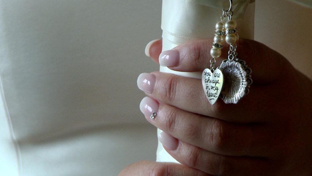 you are always in my heart locket hanging by the brides fingers as she holds her wedding bouquet tied in ivory ribbon tightly before getting married