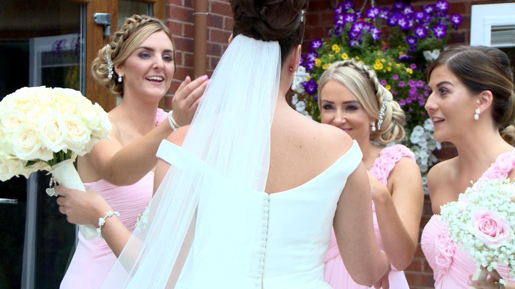 3 brides maids gush over their bride as they see her for the first time. They all look so happy for her as one reaches out to admire her earrings on the wedding video