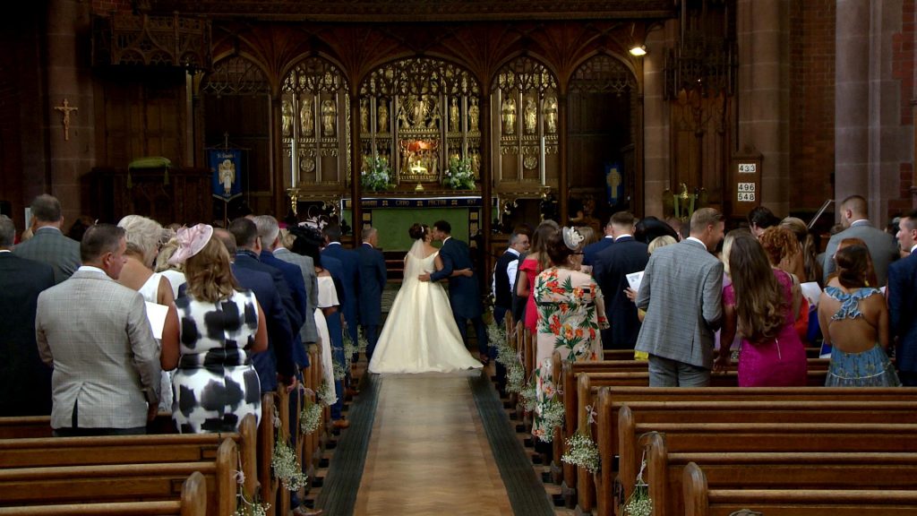 the groom greets his bride with a kiss after she's walked down the traditional church aisle at St Saviours in Birkenhead