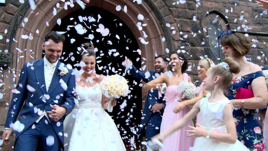 a bride and groom are showered in biodegradable pink and white confetti outside Saviours church in Oxton Wirral for their wedding video