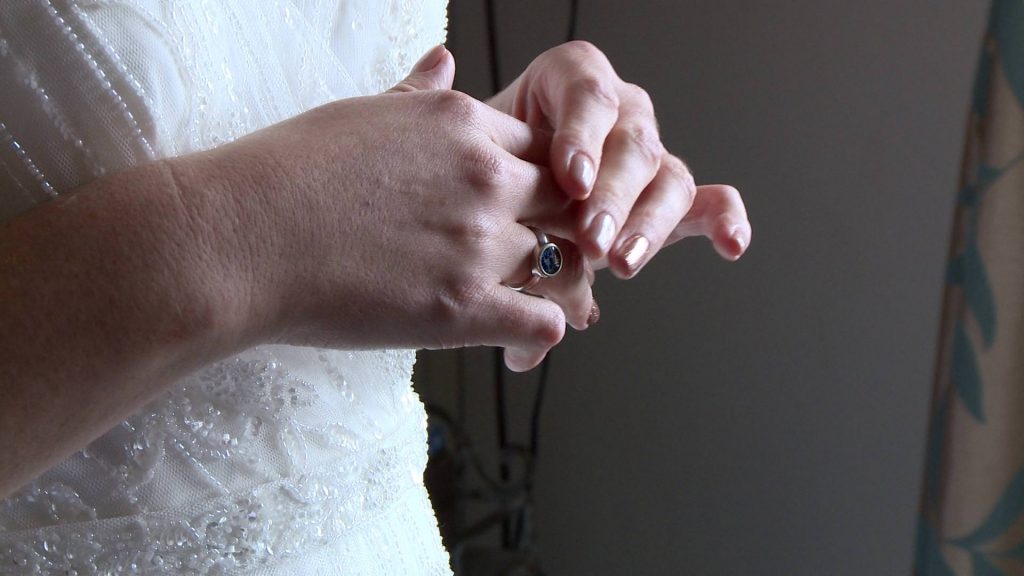 a close up of the brides hands as she plays with her silver ring. it has a blue stone and is made from the ashes of her mum who can't be at the wedding at abels harp