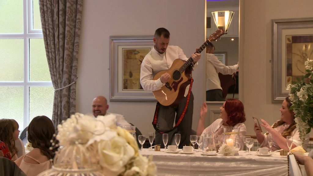an usher stands on a white wedding chair pretending to play the guitar for the wedding video