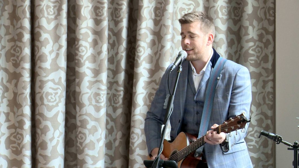 alex birtwell singing and playing acoustic guitar for a bride walking down the aisle at Alma Lodge in Stockport