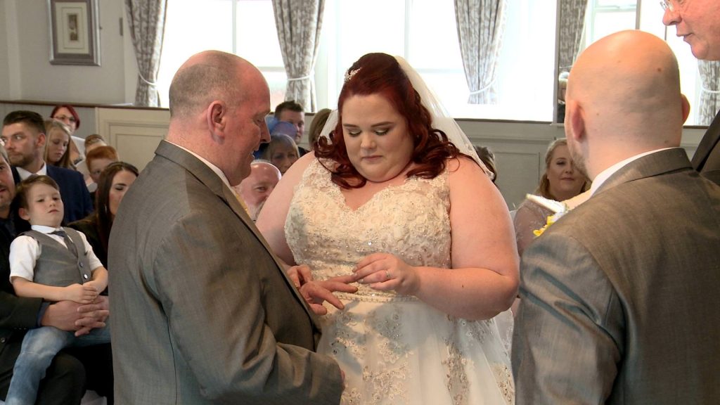 the bride places her grooms wedding ring on his finger during their Alma Lodge wedding ceremony