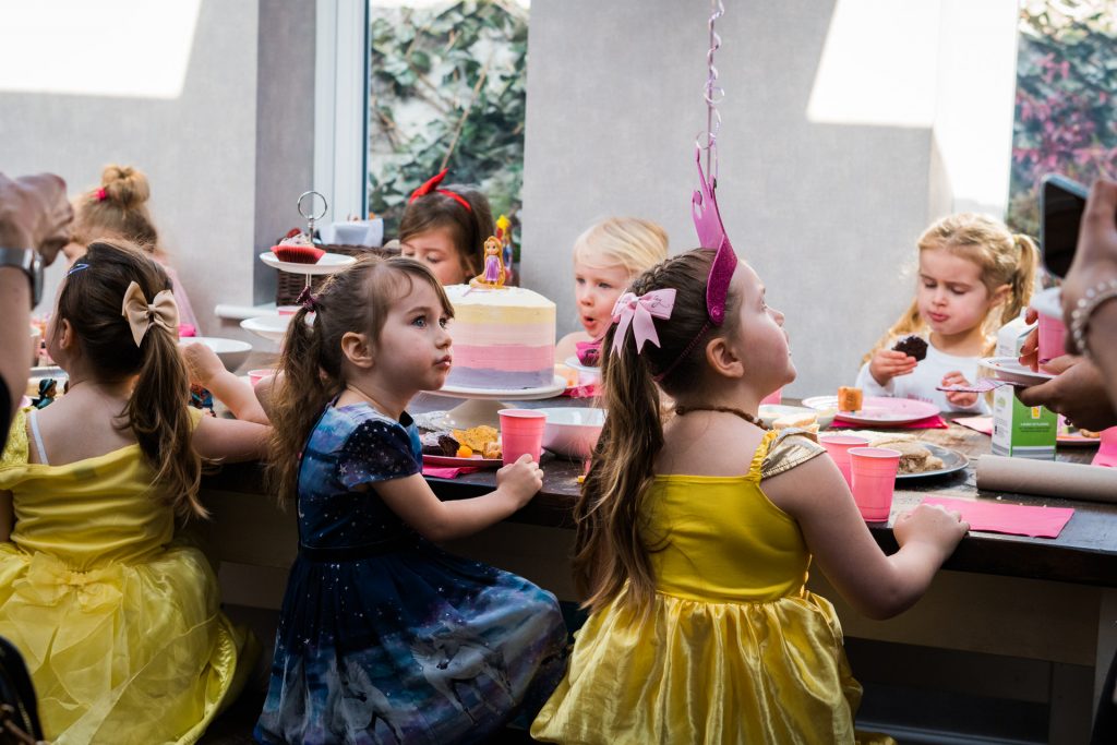 a group of young girls sit around a large dining table in a family home in Burscough eating their party food and waiting to cut the birthday cake. They're all wearing disney princess dresses for the party in Lancashire