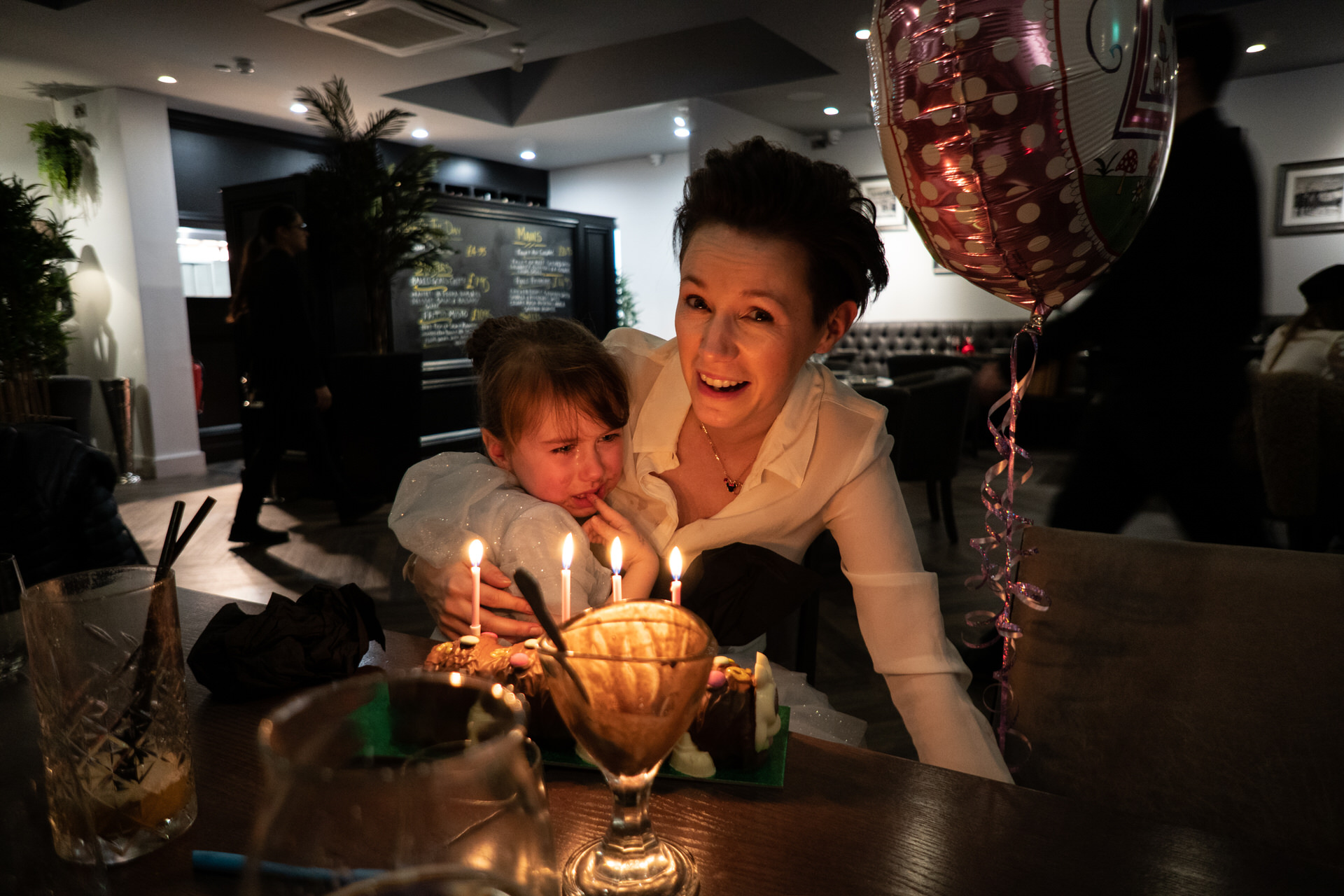 real life photo of mum cuddling crying child during birthday meal
