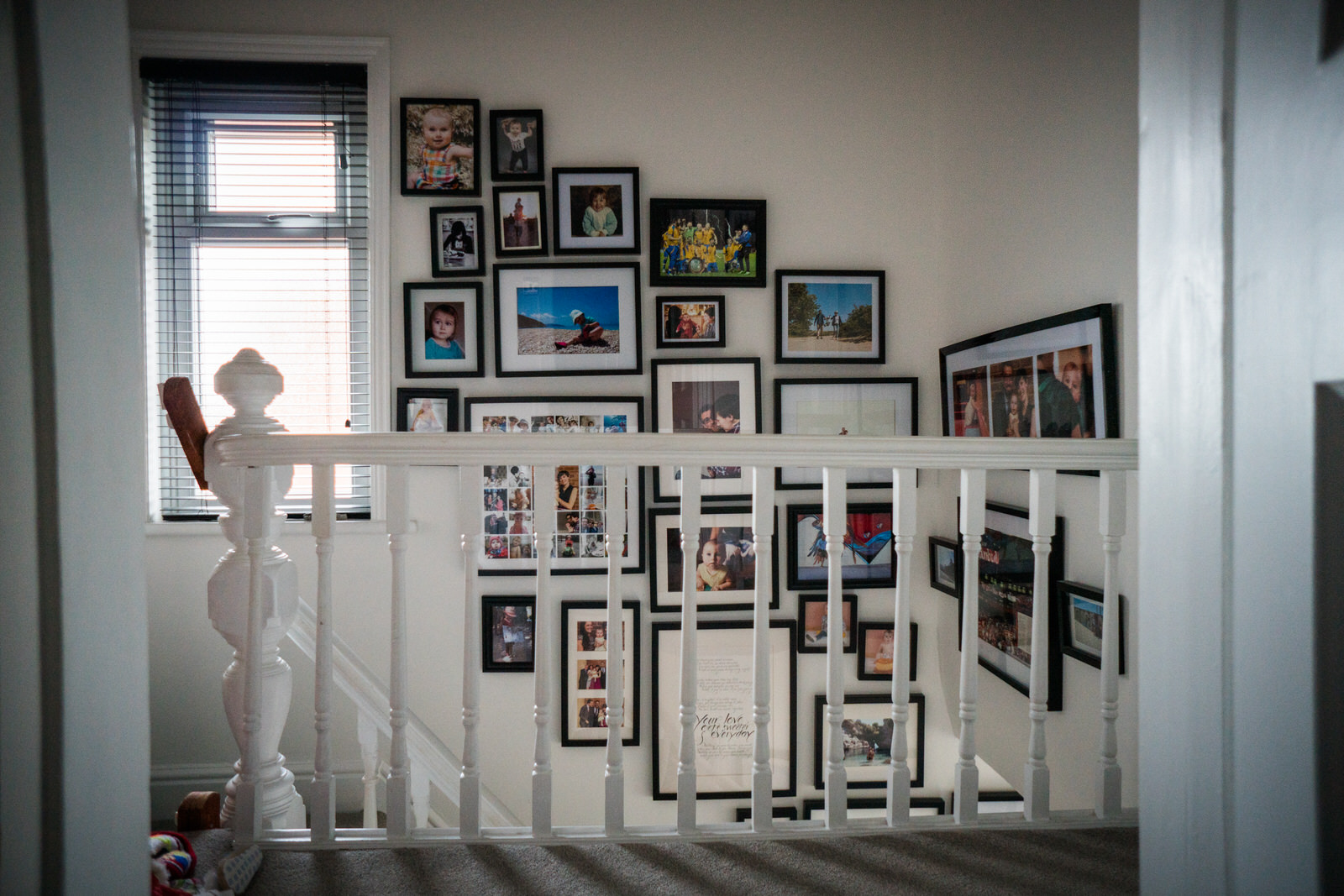 A wide shot of the top of the staircase in a family home showing off a full black framed gallery wall of family and holiday photographs in Lancashire