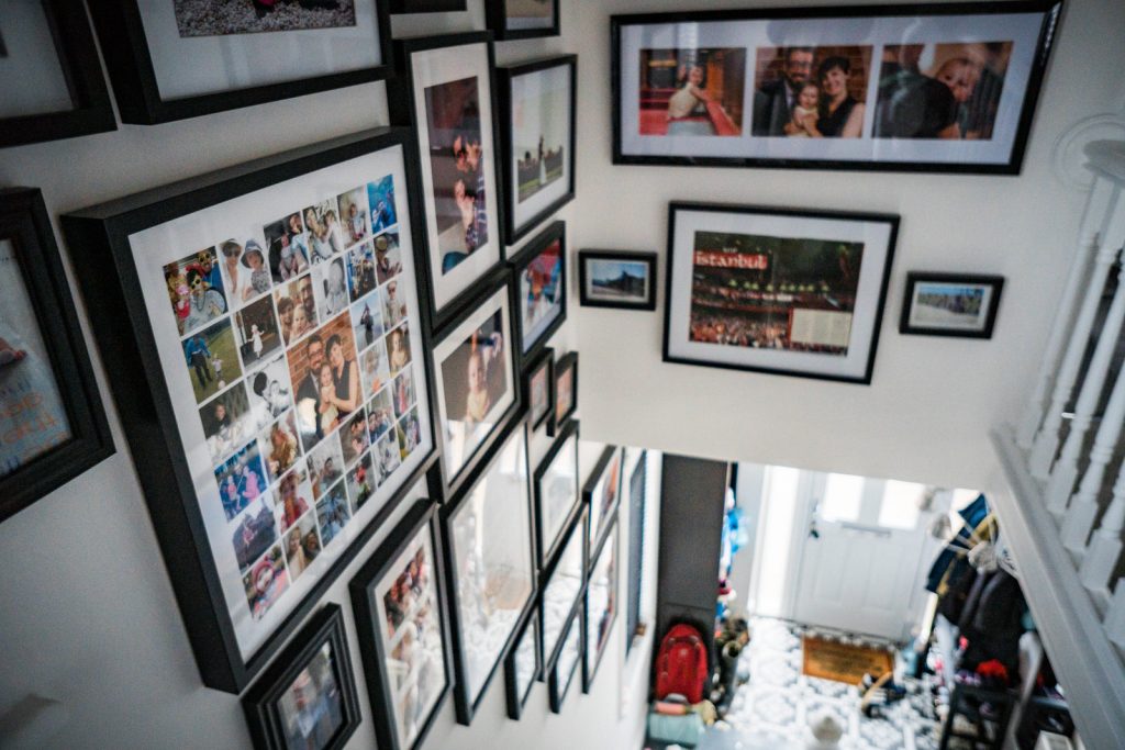looking down the stairs to the front door we can see a colelction of chunky black picture frames with a variety of personal and professional family photographs framed in a feature photo wall at a home in Lancashire
