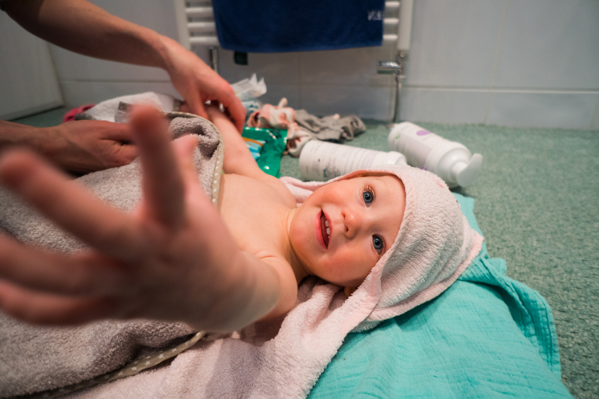 a baby girl reaches out for the camera as she gets dried off with a pink towel after her bath at home in Hale