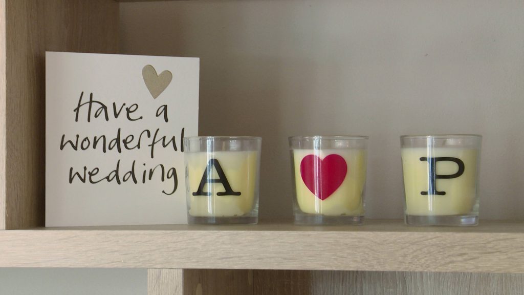 3 candles sit on a shelf next to a wedding card with the bride and grooms initials on
