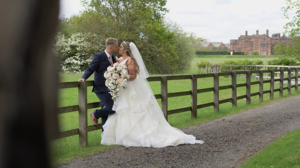 a still from the wedding video of the bride and groom having a kiss with the main house at thornton manor in the background