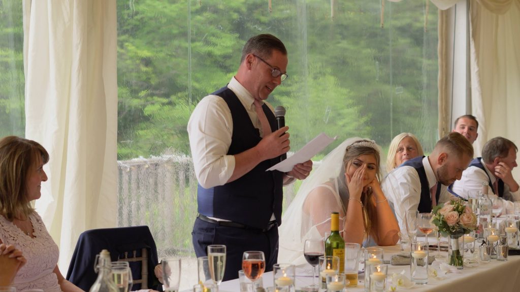 a still from the wedding video of a bride wiping away a tear during a father of the bride speech at lakeside thornton manor