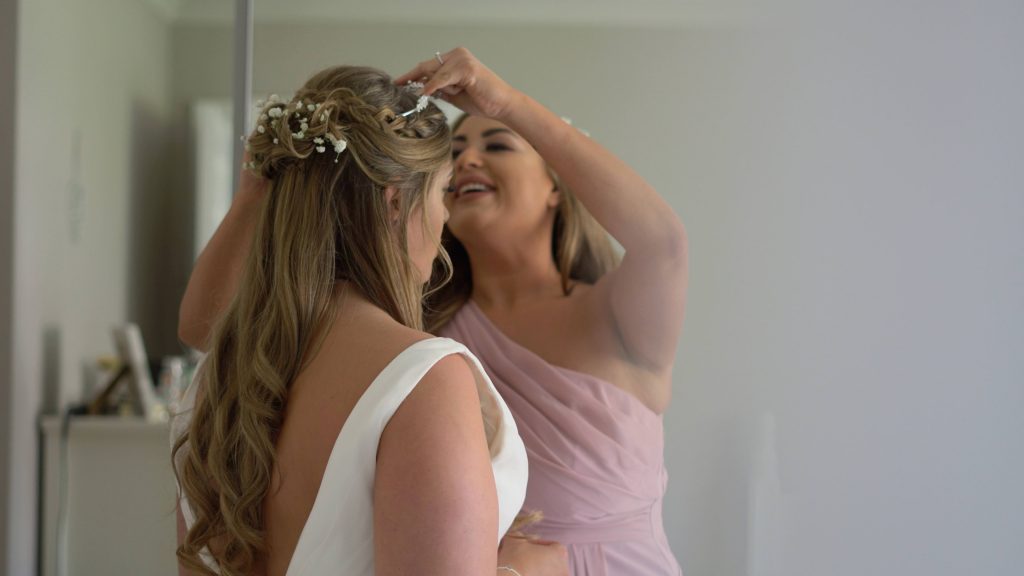 a bridesmaid wearing blush pink helps the bride with her wedding tiara hairpiece before she gets married in the wirral