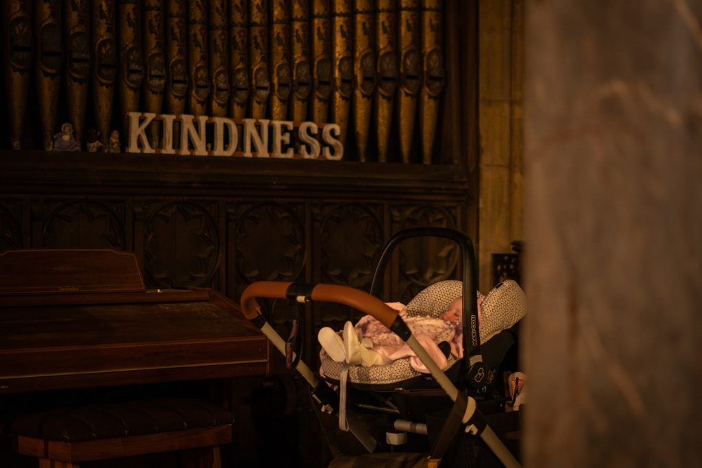 a baby girls sleeps in her pram before her family christening with the words 'kindness' in the background at the Unitarian church in Todmorden Lancashire