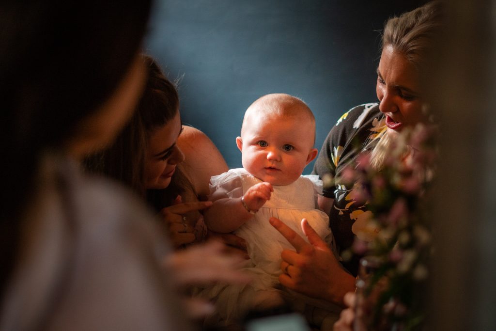 a close up of a newly christening florenece sitting with a group of women fussing over her during her christening reception at Site Pizzeria in Todmorden