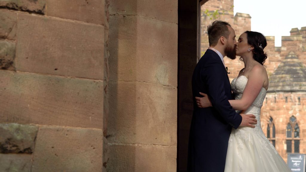 a bride and groom stand under the archway gatehouse outside peckforton castle in cheshire for some romantic shots