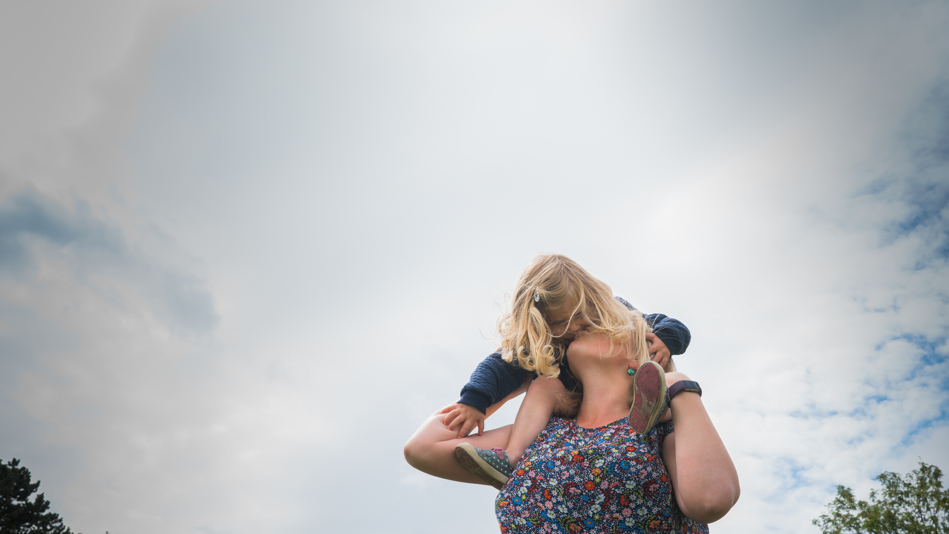a little girl on her mums shoulders leans down and kisses her mum during a family photography shoot in wetherby