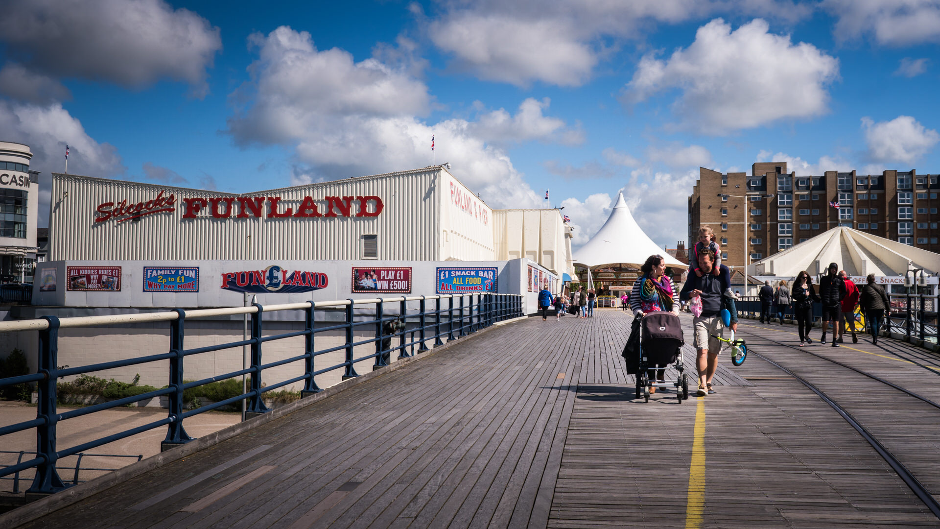 a documentary family photograph of a family walking down Southport Pier in the sunshine