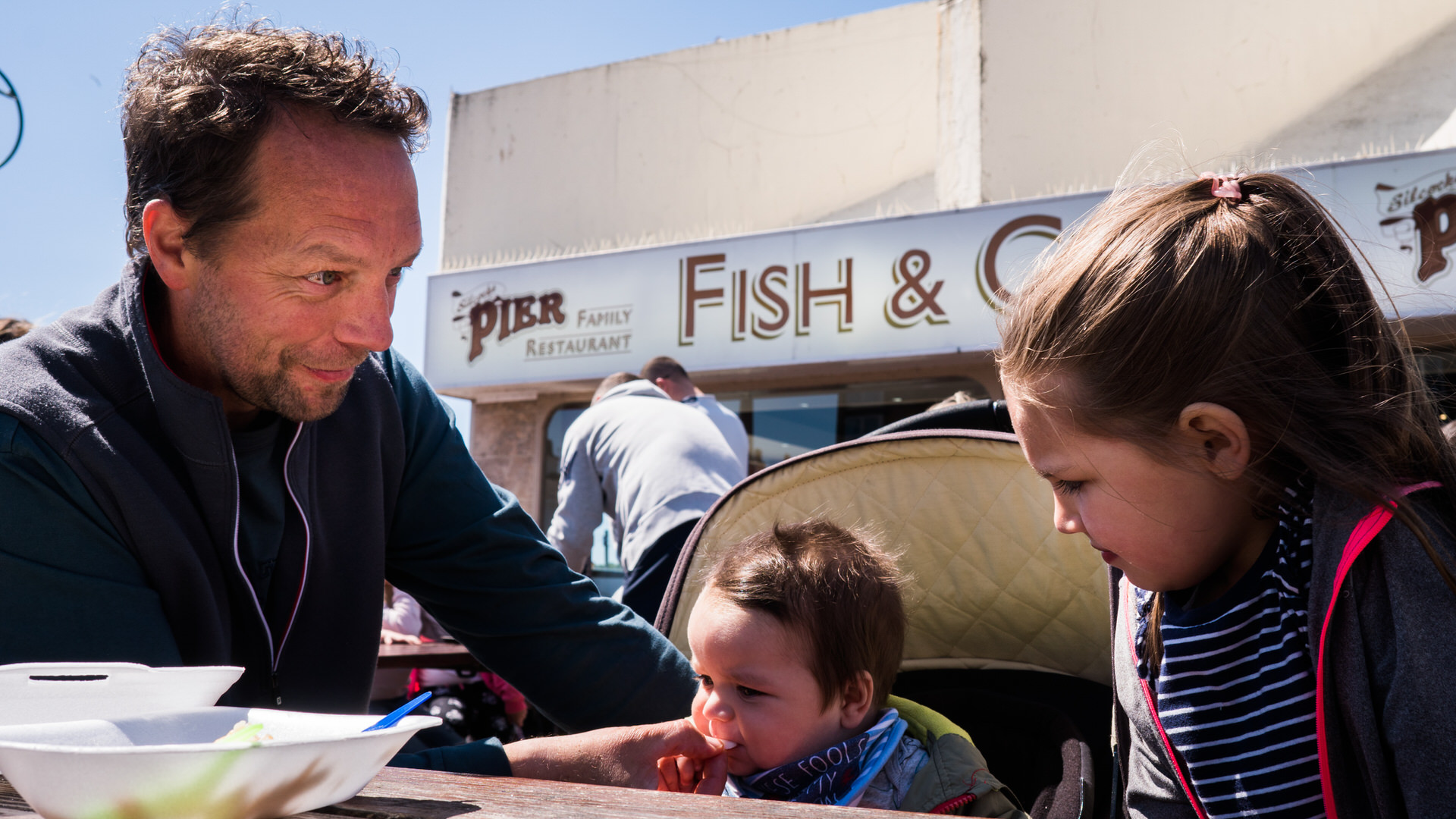 a dad feeds a baby chips at the pier in Southport during a family day out