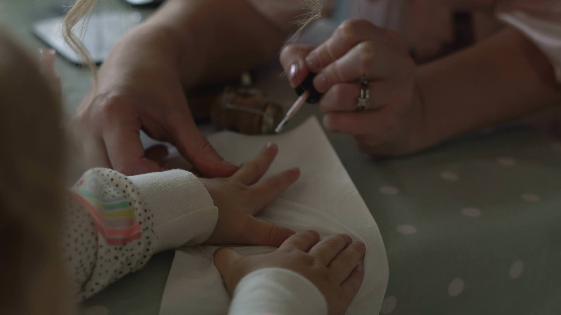 a wedding video still of a little flower girl having her nails painted