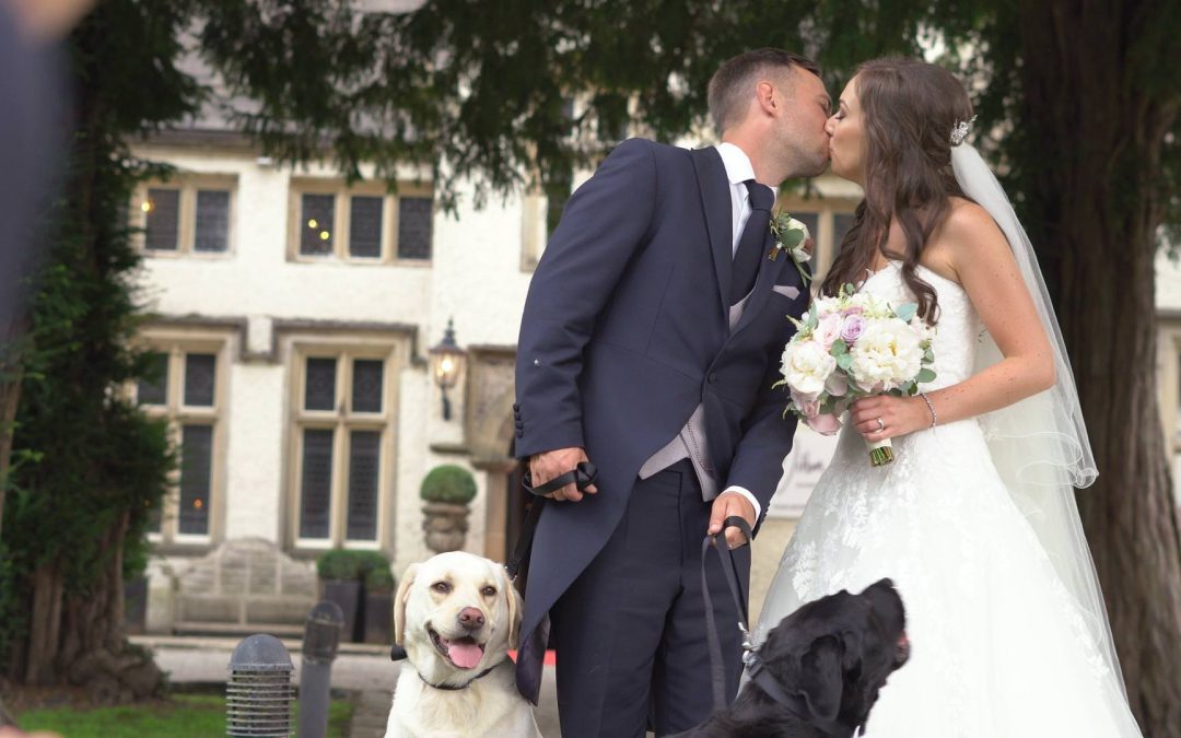 a bride and groom kiss for a photo outside Mitton Hall with their two Labradors