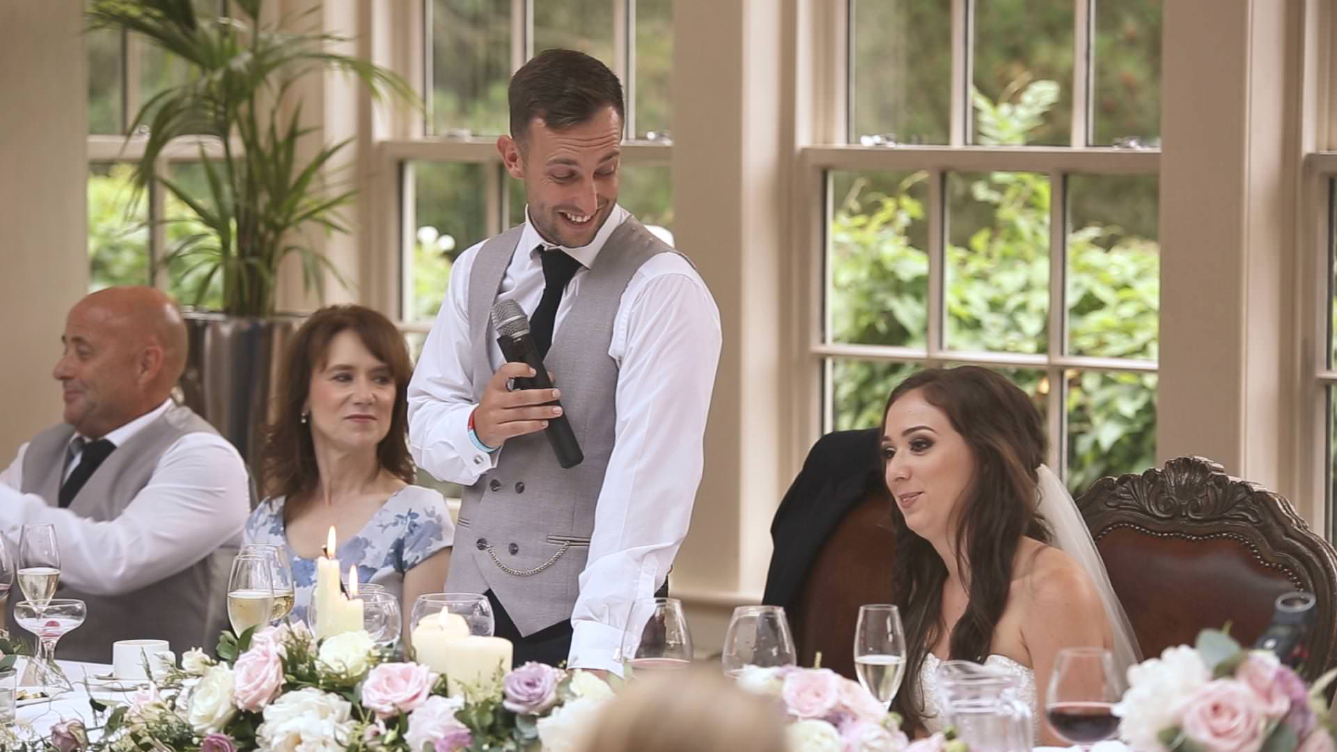 a groom smiles at his bride during his speech at Mitton Hall