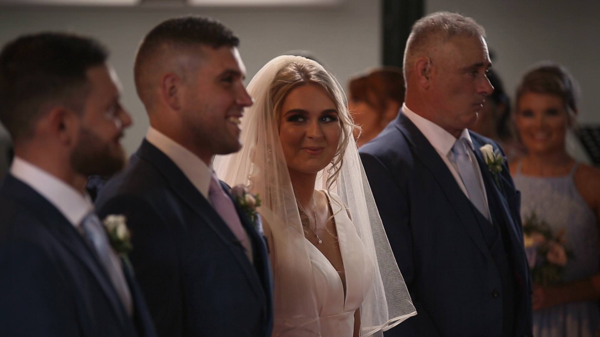 a wedding video still of a bride looking at her groom and smiling during the ceremony at St Johns church
