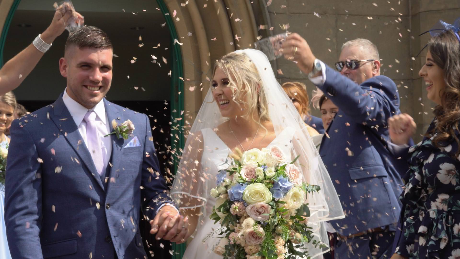 a wedding video still outside St Johns Church as they walk through confetti