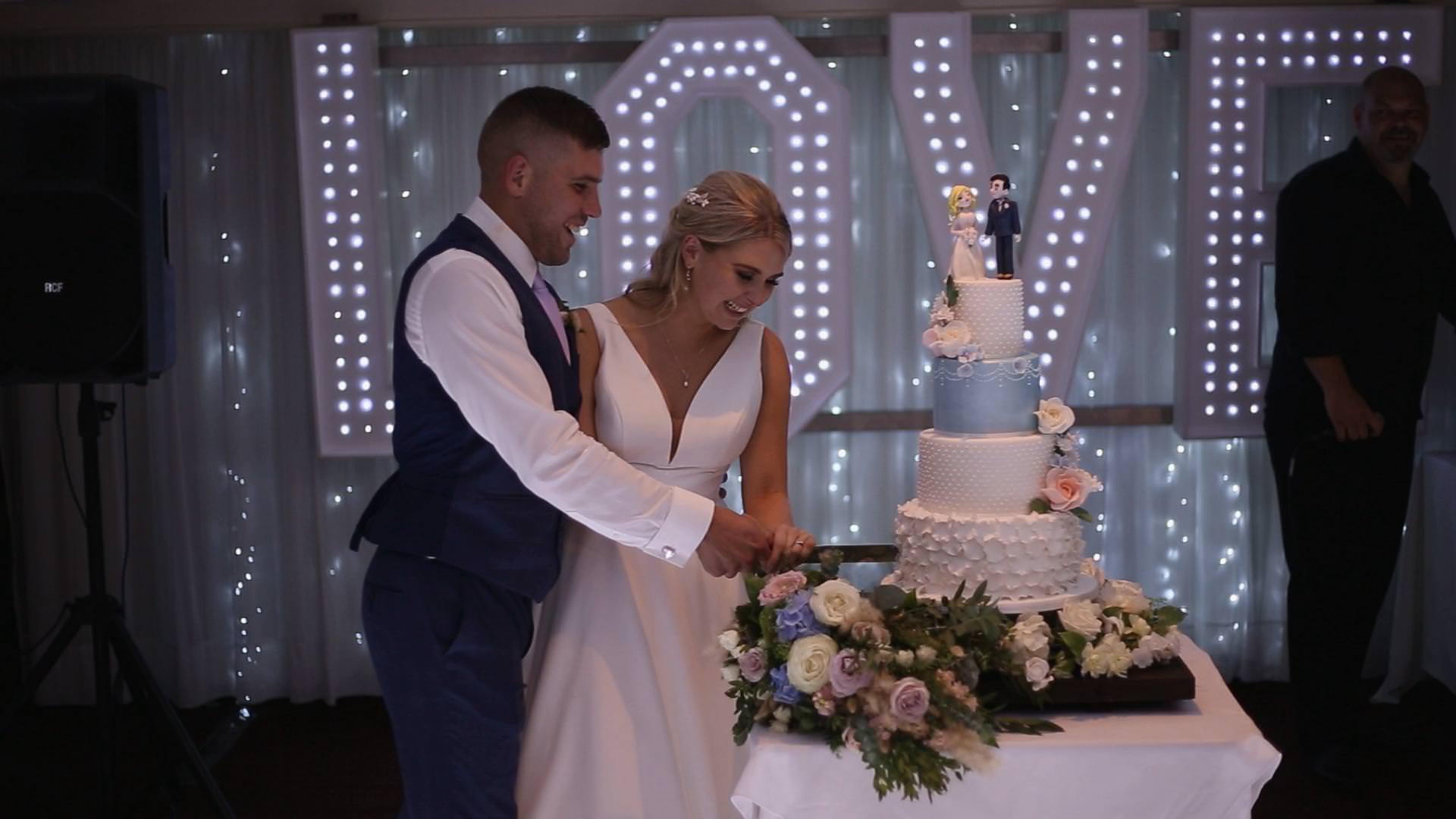 a bride and groom smile as they cut their 4 tier wedding cake at Briars Hall