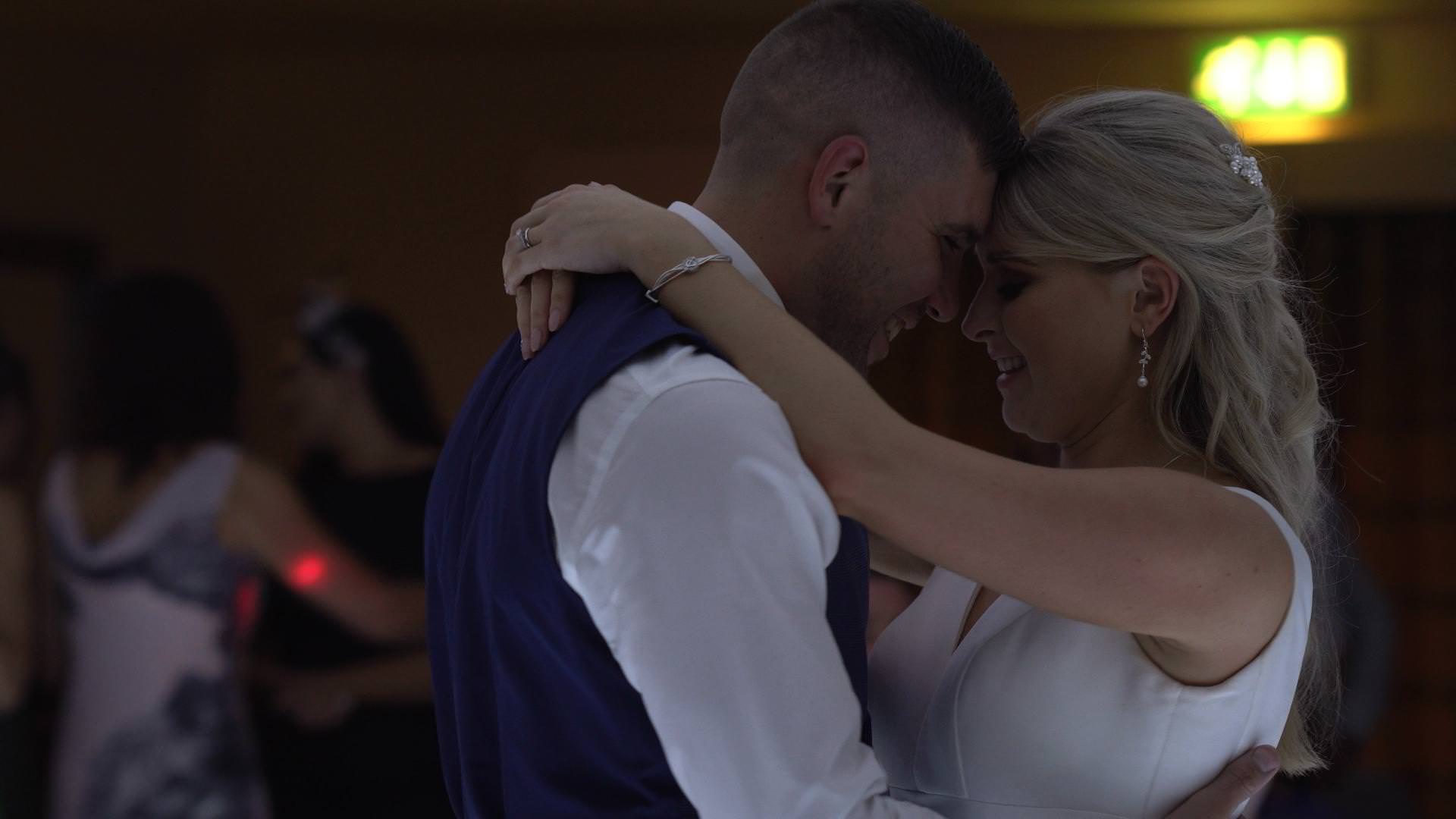a wedding video still of a bride and groom touching heads during their first dance