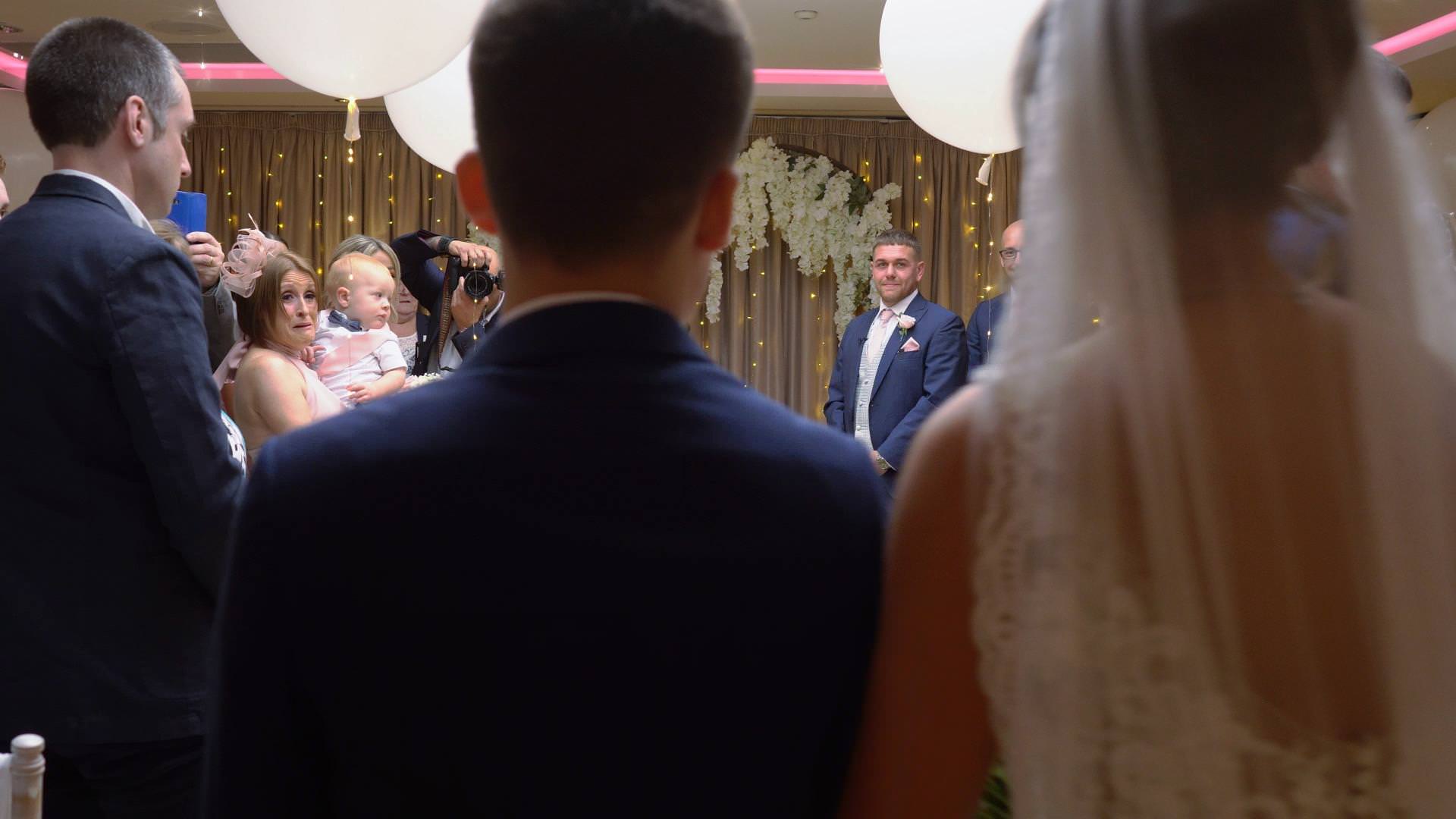 Video still of a groom turns to see his bride walk down the aisle at Moddershall Oaks